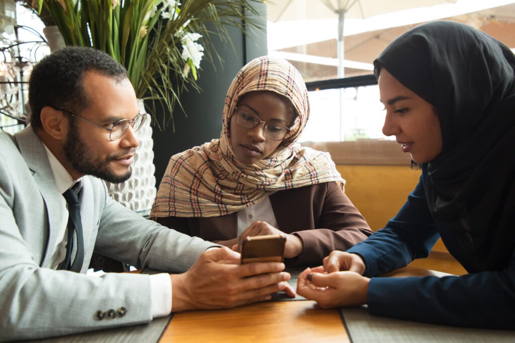 Multicultural coworkers enthusiastically watching something on mobile device